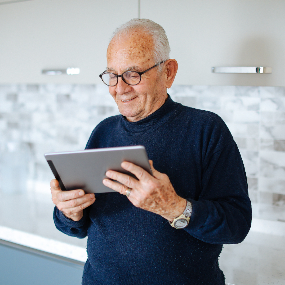 oudere man met een tablet in zijn handen, waarnaar hij aandacht kijkt