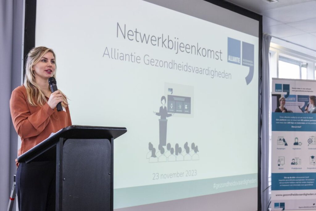 Foto van een vrouw die een presentatie geeft bij een netwerkbijeenkomst van de Alliantie Gezondheidsvaardigheden van Pharos