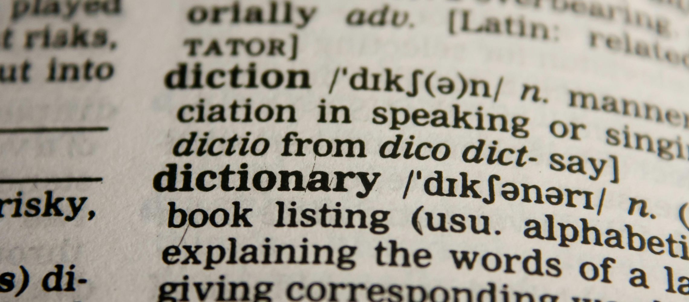 De afbeelding toont een close-up van een woordenboekpagina. Je ziet de Engelse woorden 'diction' en 'dictionary' in vetgedrukte letters, met daarachter de fonetische uitspraak en een korte uitleg van de betekenis.