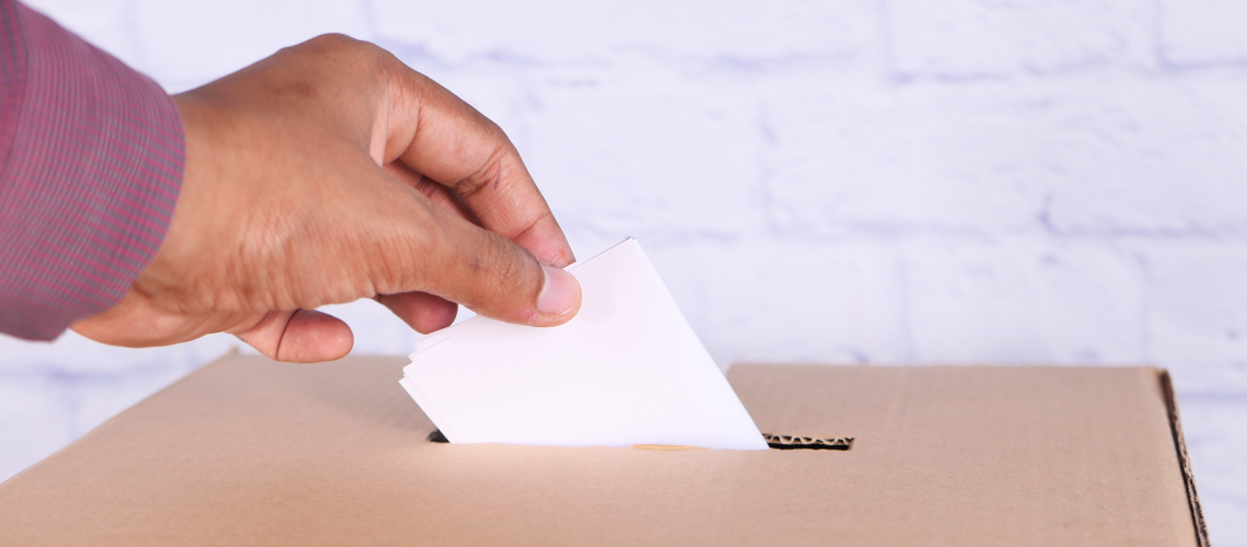 foto van een hand die een stembiljet in een doos stopt